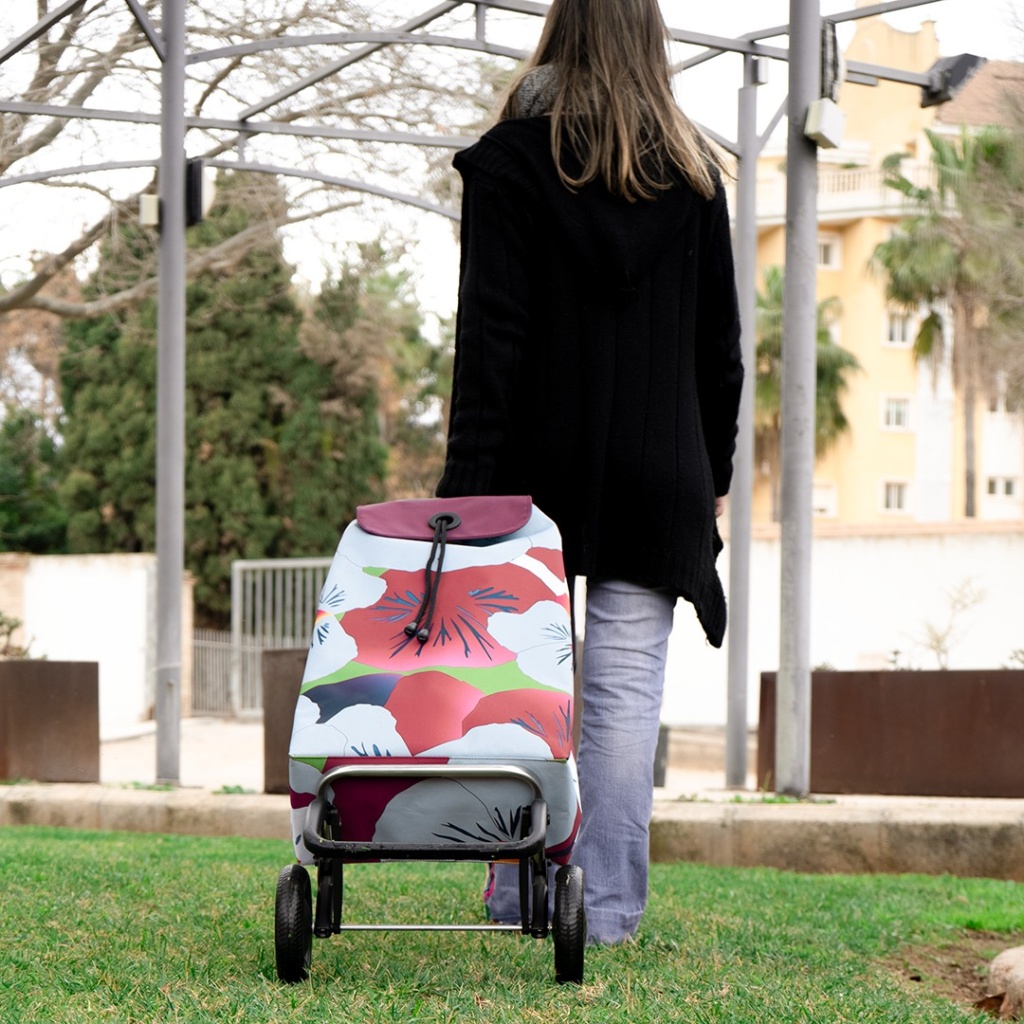 une femme marche avec un chariot Rolser Imax 2 roues taku à fleurs rouge et rose